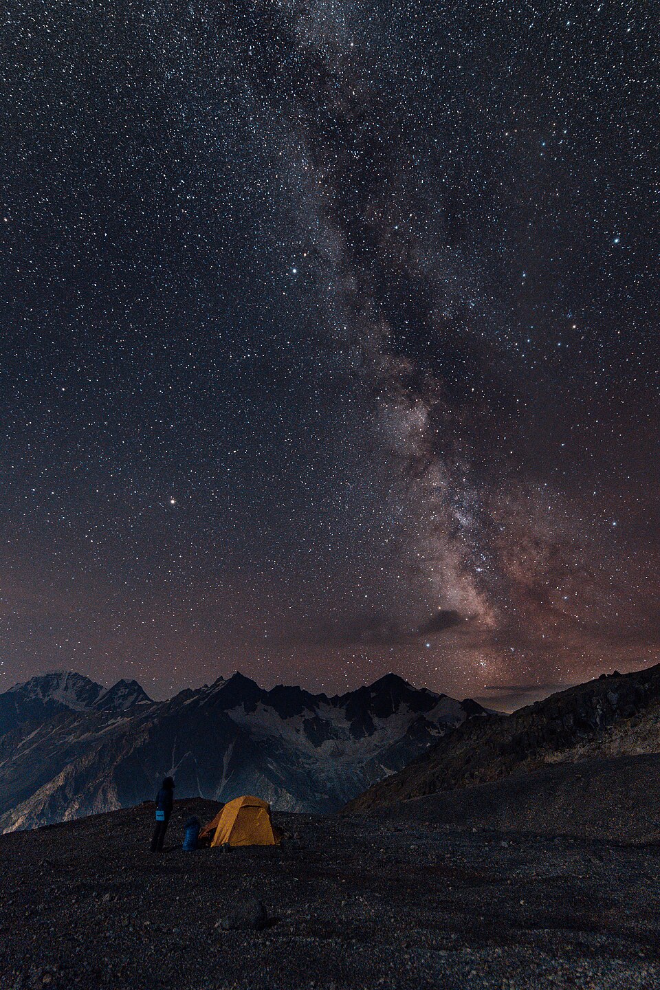 Backpackers pitch a tent on a mountainside beneath the mily way